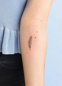 a woman's arm with a small feather tattoo on the left side of her arm