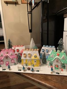 a table topped with lots of small toy houses covered in frosted snow next to a refrigerator