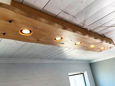 a wooden beam with four lights hanging from it's side in an empty room