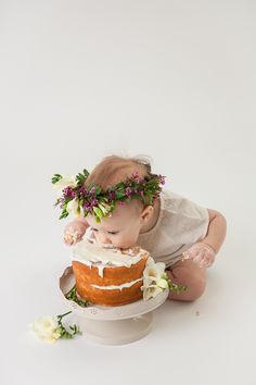 a baby is sitting on the floor with a cake in front of her face and wearing a flower crown