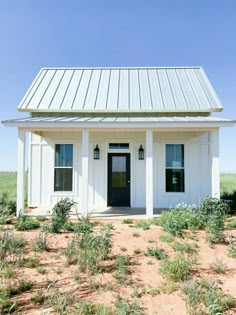 a small white house with a metal roof and black doors in the middle of nowhere