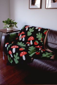 a couch covered in a mushroom blanket next to a table with two pictures on it