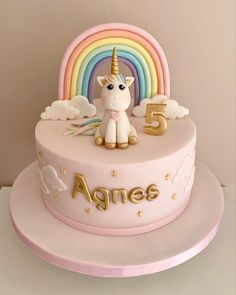 a pink cake with a unicorn on top and rainbows in the background that says age 5