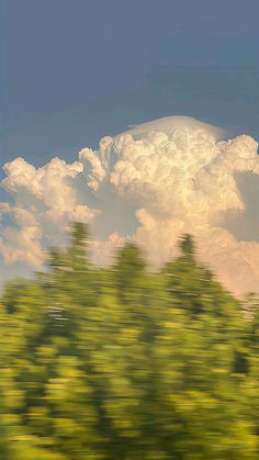 the sky is very cloudy and there are many trees in front of it, as seen from a moving train