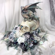 a dragon statue sitting on top of a pile of skulls and flowers in front of a white curtain