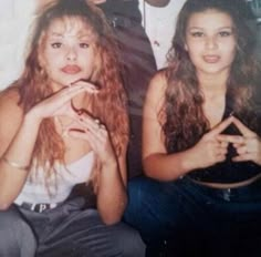 two women sitting next to each other with one holding her hand on her chest and the other looking at the camera