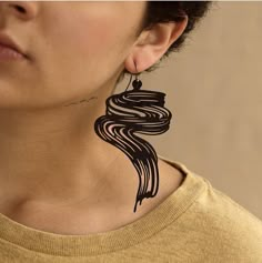 a woman wearing large black earrings with swirl designs on her face and neck, standing in front of a beige wall