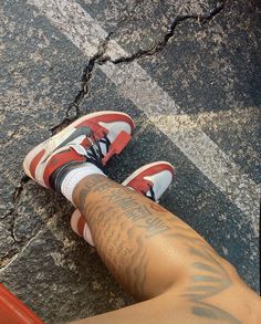 a person has tattoos on their legs and is sitting in front of an orange pole