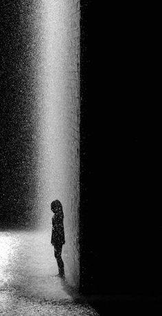 a black and white photo of a person standing in front of a water fountain at night