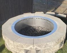 an outdoor fire pit sitting on top of grass next to a fenced in area