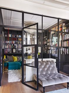 a living room filled with lots of furniture and bookshelves covered in glass doors