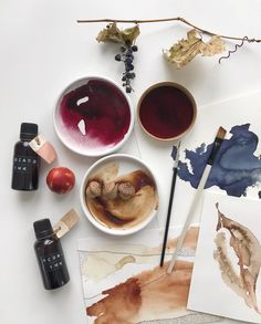 various paints and brushes are sitting on the table next to each other, including watercolors