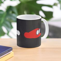 a black and red coffee mug sitting on top of a wooden table next to a book