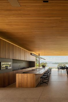 The first photo shows an open kitchen space with outside furniture, framed by a large tree. The second photo is a closer shot of the kitchen from the side, where you can see a long island with bar stools, with the oven, sink and counter space lining the back wall. You can see a large dam in the distance from the open side of the space. The third and final photo is another close up shot of the kitchen, straight on. You can see the bar stools lining the island with the oven and counter behind. Flat Roof House, Modern Flat, House Roof, House Inspo, Summer House, Future House, Outdoor Kitchen, Architecture House