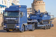 a large blue truck parked in front of a tall building with a tower behind it