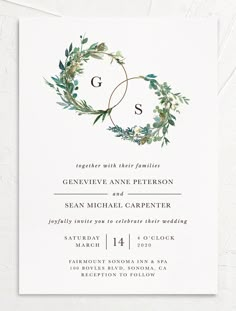 an elegant wedding card with greenery and the letter g is on top of it