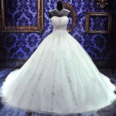 a white ball gown on display in front of a blue wall with ornate designs and framed pictures