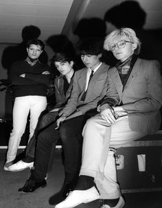 black and white photograph of four men in suits sitting next to each other on luggage