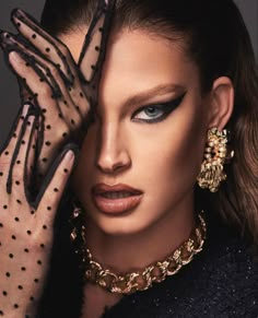 a woman with black and gold makeup holding her hands up to her face