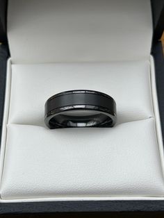 a black wedding band in a box with the lid open and its reflection on it