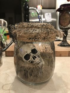 a glass jar filled with sand and a skull on the inside is sitting on a counter