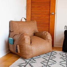 a brown chair sitting on top of a wooden floor next to a black bag and suitcase