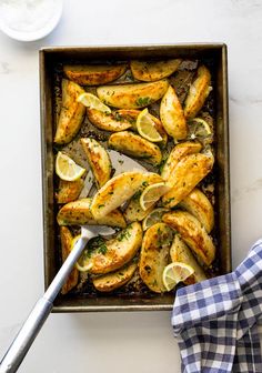 a baking pan filled with baked potatoes and lemon wedges on top of a table