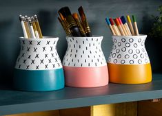 three vases with pens and pencils in them on a shelf