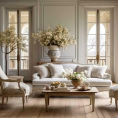 a living room with white furniture and flowers in the vase on the coffee table next to the couch