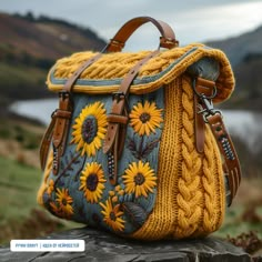 a yellow and blue handbag sitting on top of a rock in front of a lake