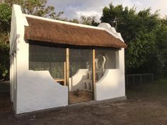 a small white building with a thatched roof and two cats in the doorways