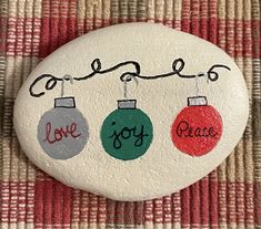 three ornaments on a rock with the words love, joy and peace painted on them