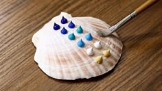 a small seashell with blue, white and yellow drops on it next to a paintbrush