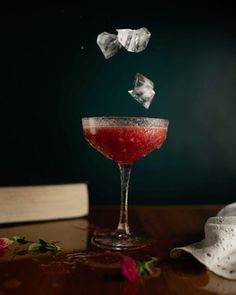 a glass filled with liquid sitting on top of a wooden table next to an open book