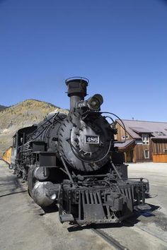 an old fashioned train is parked on the tracks in front of a mountain side house