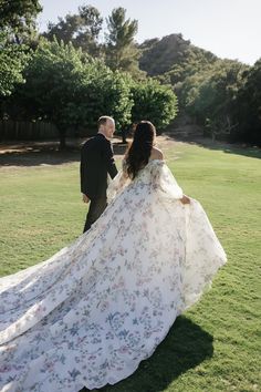 the bride and groom are walking through the grass in their wedding gowns with floral print on them