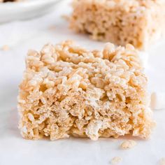 two pieces of rice krispy treats sitting on top of a white countertop next to another piece of cake