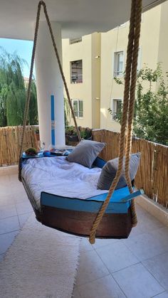 a bed suspended from a rope in front of a building with pillows on the bottom