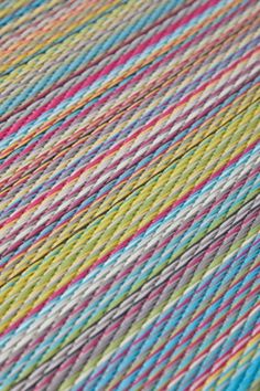 multicolored yarn is laying on top of a tablecloth with white, blue, pink, yellow and green stripes