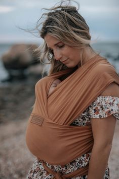 a woman wearing a brown wrap around her waist on the beach with rocks in the background