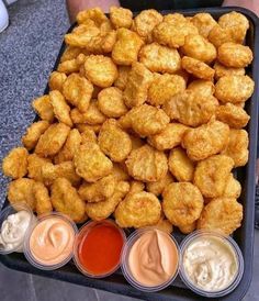 a tray filled with tater tots next to dipping sauces and ketchup