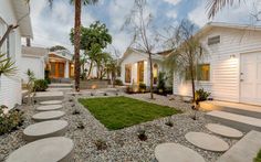 a white house with lots of plants and rocks in the front yard, surrounded by palm trees