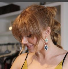 a woman in a yellow top looking at her cell phone while wearing earrings