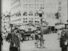 an old black and white photo of people walking on the street in front of buildings