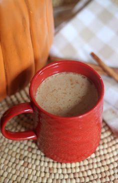 a red mug filled with liquid sitting on top of a table next to a pumpkin