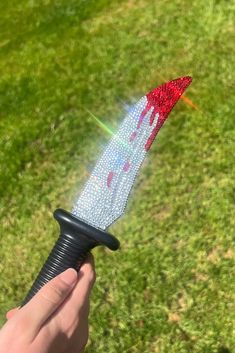 a hand holding a black and red fire extinguisher on top of green grass