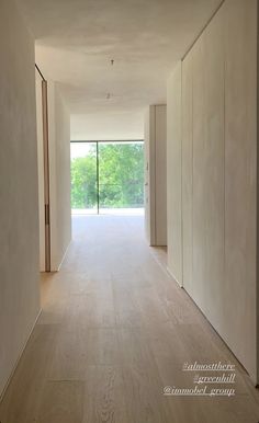 an empty room with white walls and wood floors is seen from the hallway to the outside