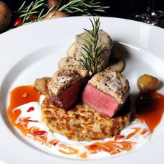 a white plate topped with meat covered in sauce and garnished with green sprigs