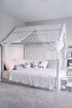 a white canopy bed sitting in a bedroom next to a book shelf filled with books