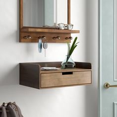 a wooden shelf with a mirror and vase on it next to a blue door in a white room